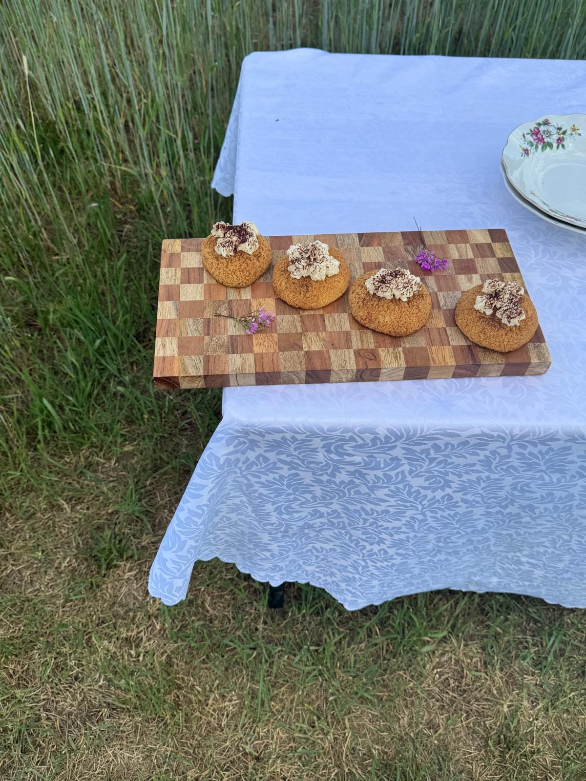 Cream-topped choux pastries arranged on a wooden board outdoors